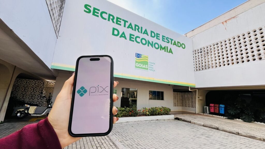 Celular com o logotipo do Pix em frente à fachada da Secretaria de Estado da Economia de Goiás