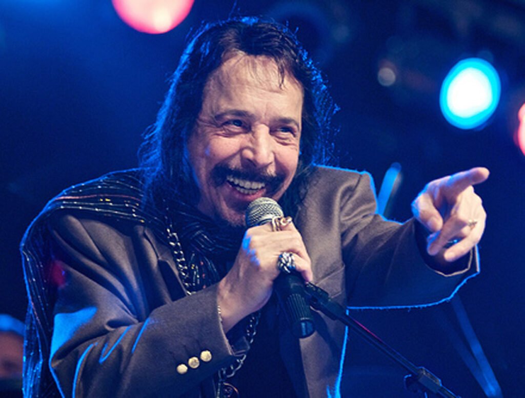 O cantor Benito di Paula sorri e aponta para a plateia com o microfone na mão durante show