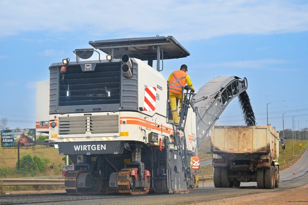 Máquina fresadora retira o asfalto antigo e despeja o material em caminhão durante obra de restauração da GO-020